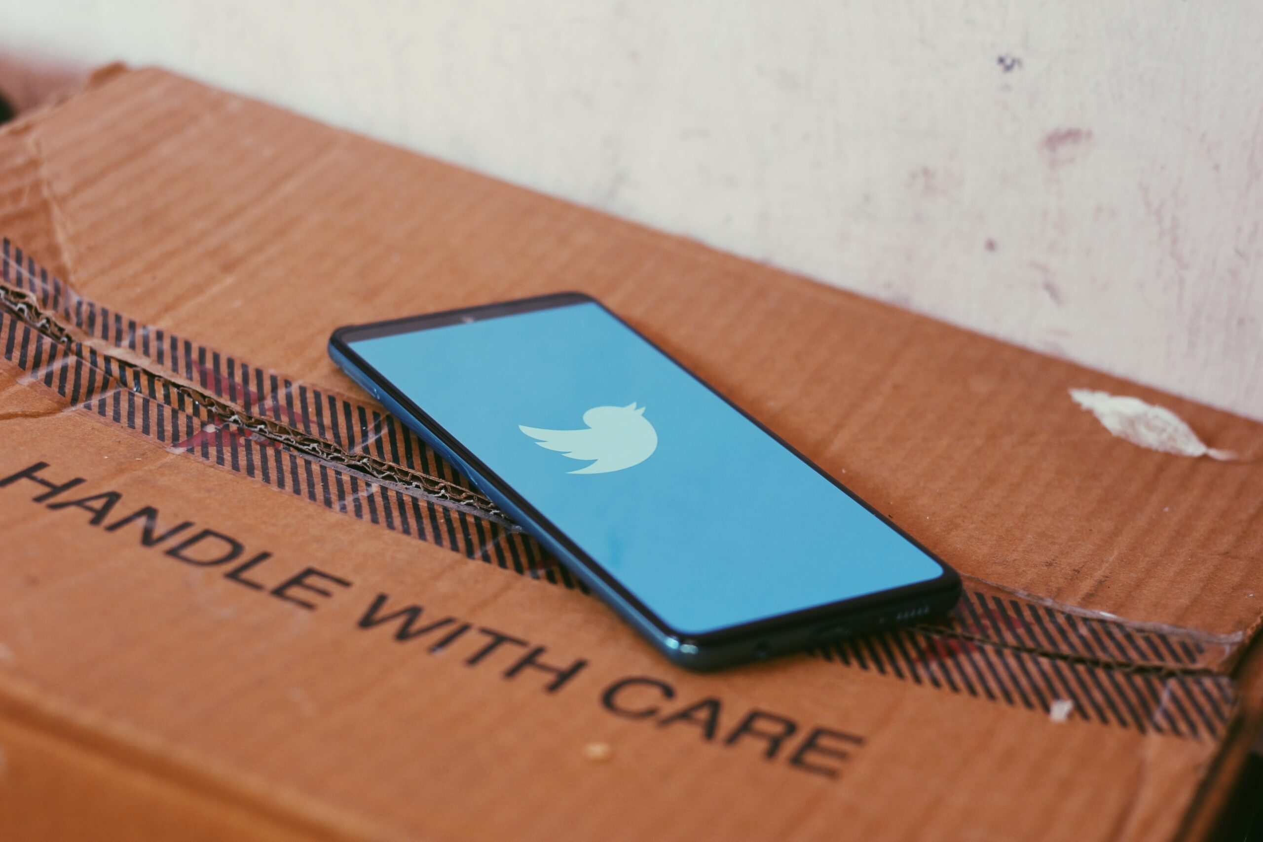 Phone with Twitter logo on the screen sat on 'handle with care' box